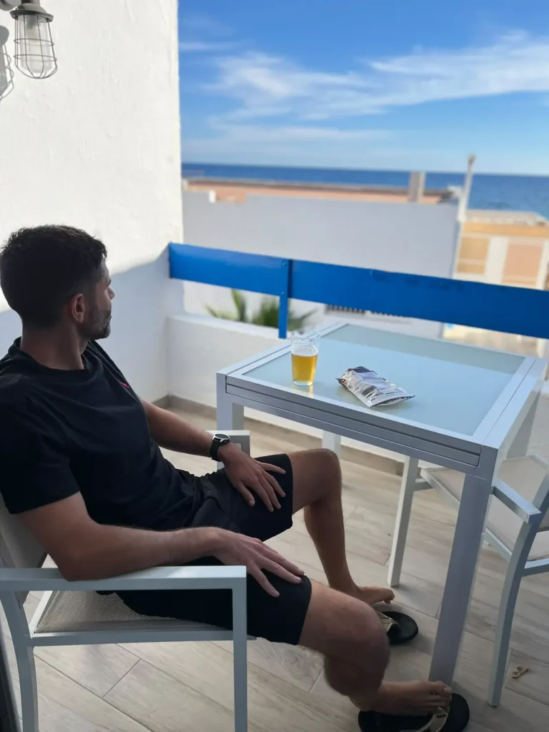 Pablo descansando en una terraza con vistas al mar después de la carrera, con un vaso y una bolsa de patatas en la mesa.