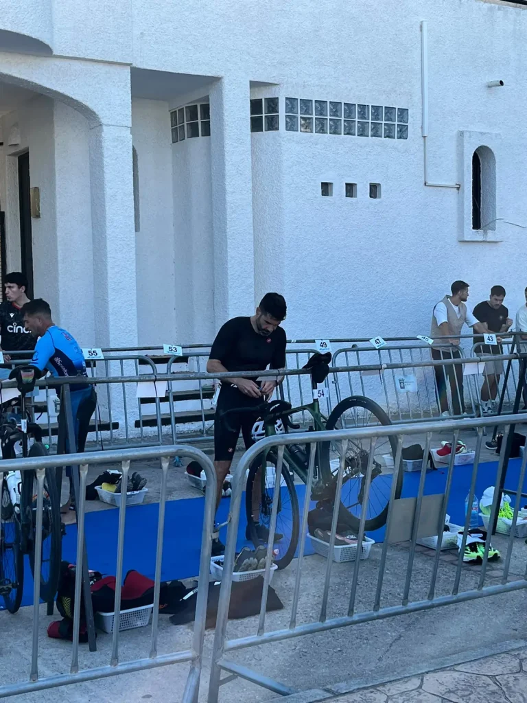 Pablo preparando su bici verde en su sitio de la T1, con el tritraje negro, entre barreras metálicas.