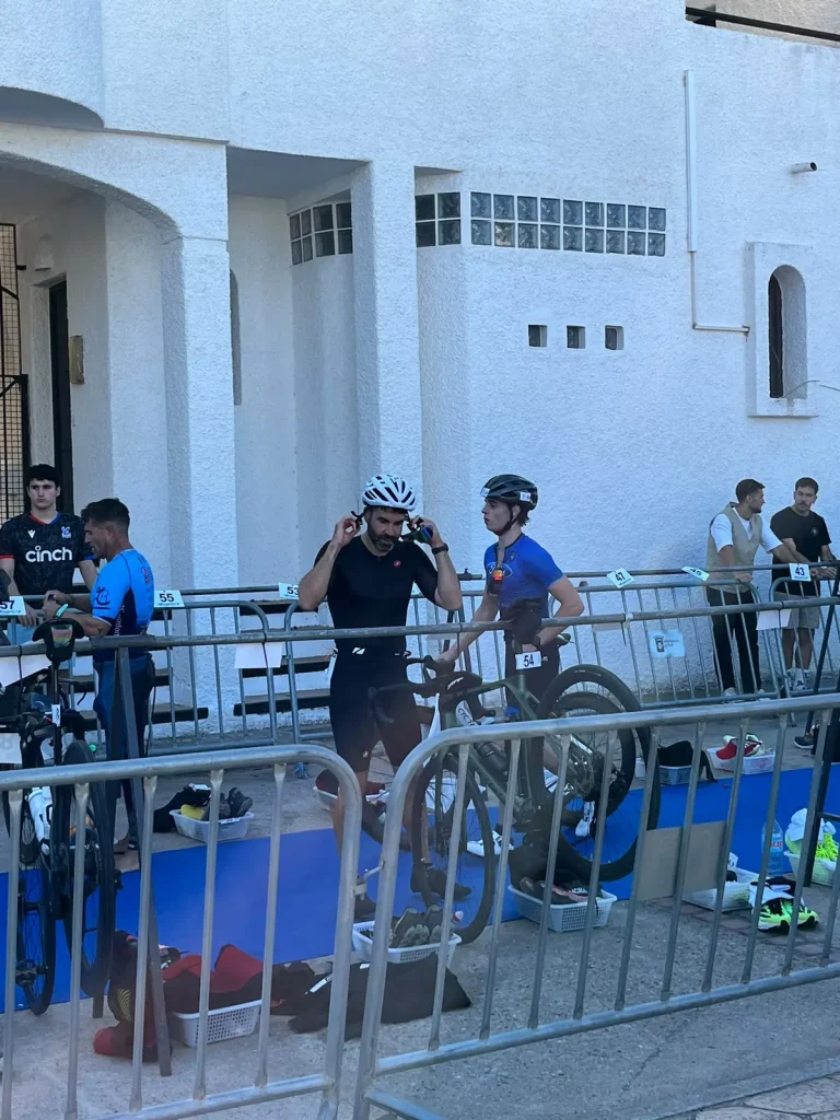 Pablo abrochándose el casco blanco en la T1, ya con las zapatillas de calas, junto a su bici y entre otros triatletas.